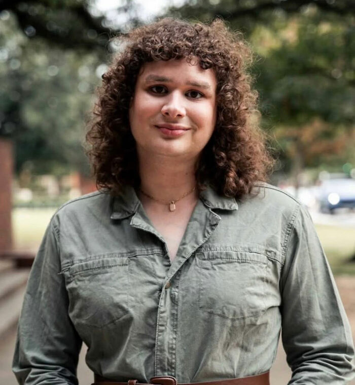 Person with curly hair wearing a green button-up shirt outdoors, related to trans instructor ousted from college topic