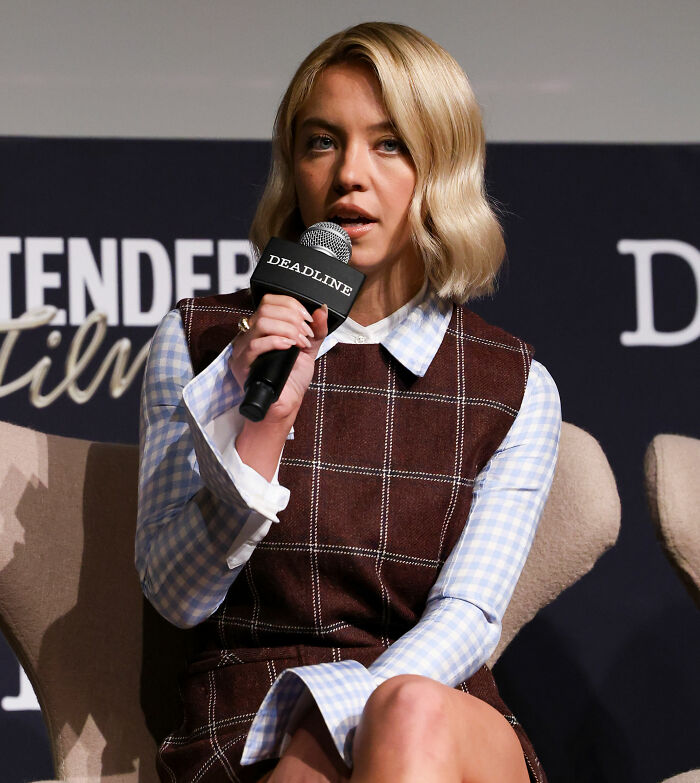 Sydney Sweeney speaking at a panel event, holding a microphone with Deadline logo, discussed her pairing with Ethan Hawke.