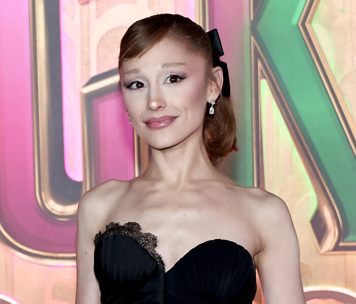 Ariana Grande posing in a black strapless dress with earrings, attending a colorful event background. Ariana Grande posing in a black strapless dress with earrings, attending a colorful event background.