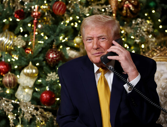 Donald Trump in a dark suit on the phone with a decorated Christmas tree in the background during holiday season. Donald Trump in a dark suit on the phone with a decorated Christmas tree in the background during holiday season.
