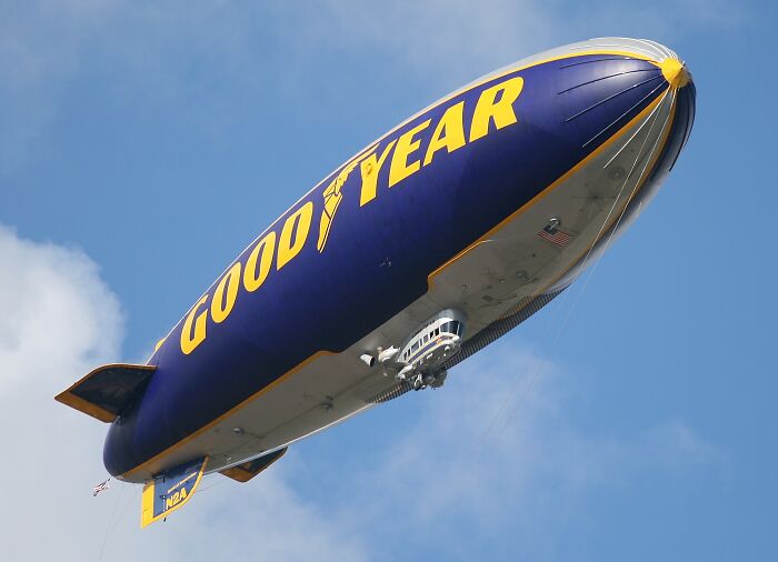 Goodyear blimp flying in clear blue sky as people share historical facts unknown until recently.