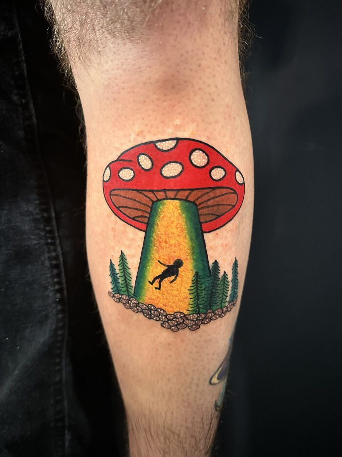 Colorful psychedelic tattoo on forearm features a red mushroom with a glowing green beam and tiny floating figure. Colorful psychedelic tattoo on forearm features a red mushroom with a glowing green beam and tiny floating figure.