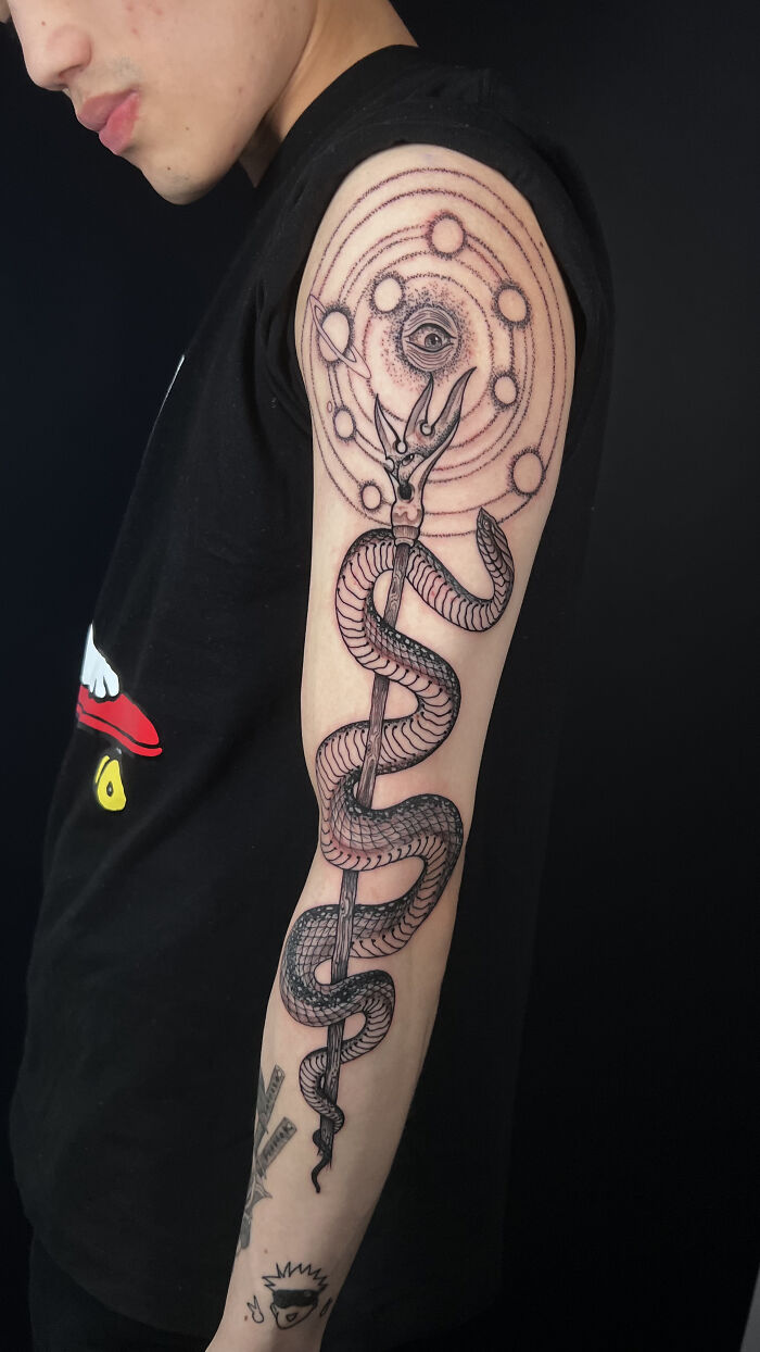 Person showing a detailed psychedelic tattoo featuring a snake, cosmic symbols, and an all-seeing eye on the upper arm. Person showing a detailed psychedelic tattoo featuring a snake, cosmic symbols, and an all-seeing eye on the upper arm.