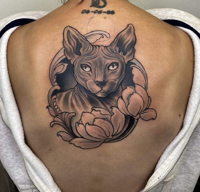 Tattoo of a detailed cat portrait with floral elements on a person's upper back, a tribute to memories of pets.