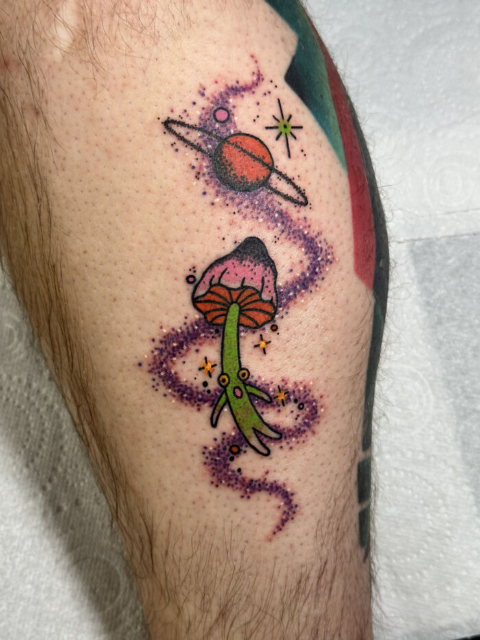 Colorful psychedelic tattoo of a mushroom and planet with stars surrounded by a swirling purple cosmic trail on skin. Colorful psychedelic tattoo of a mushroom and planet with stars surrounded by a swirling purple cosmic trail on skin.