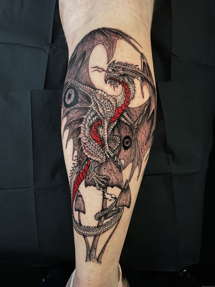 Psychedelic tattoo of a detailed dragon with red accents wrapped around mushrooms on a person’s leg. Psychedelic tattoo of a detailed dragon with red accents wrapped around mushrooms on a person’s leg.