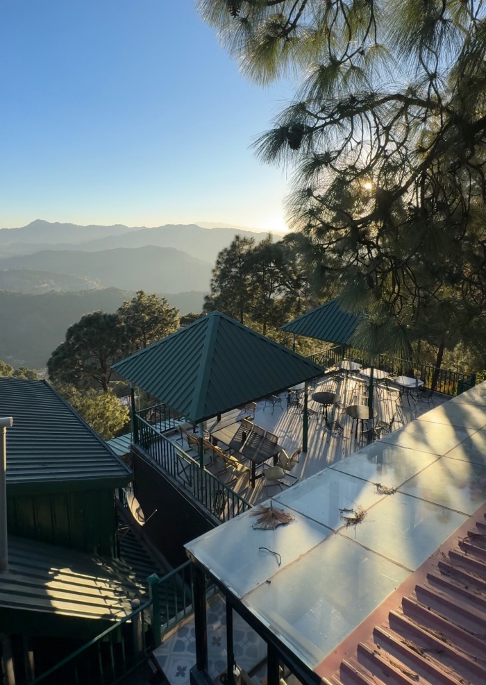 Terrace seating with green roofs overlooking pine trees and distant mountains in hidden gems of Himachal Pradesh.