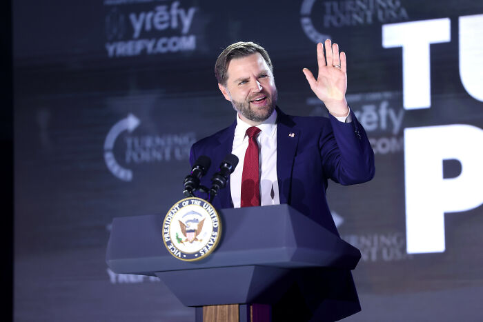 JD Vance speaking at a podium with Vice President seal, addressing marriage speculation after Erika Kirk viral hug and Usha’s bare finger.