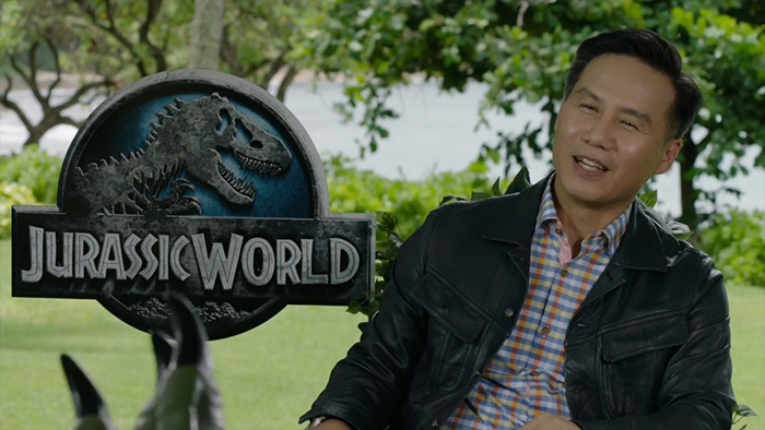 BD Wong from Jurassic World outdoors near a Jurassic World sign, wearing a black jacket and plaid shirt. BD Wong from Jurassic World outdoors near a Jurassic World sign, wearing a black jacket and plaid shirt.