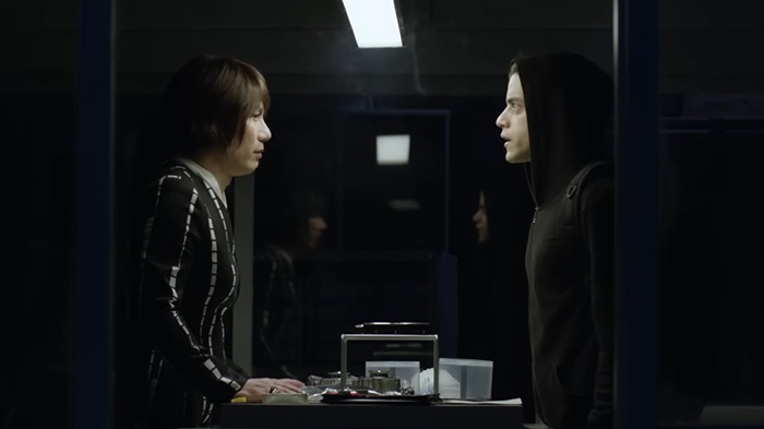 BD Wong from Jurassic World in a tense conversation wearing a striped outfit facing a person in a black hoodie indoors. BD Wong from Jurassic World in a tense conversation wearing a striped outfit facing a person in a black hoodie indoors.