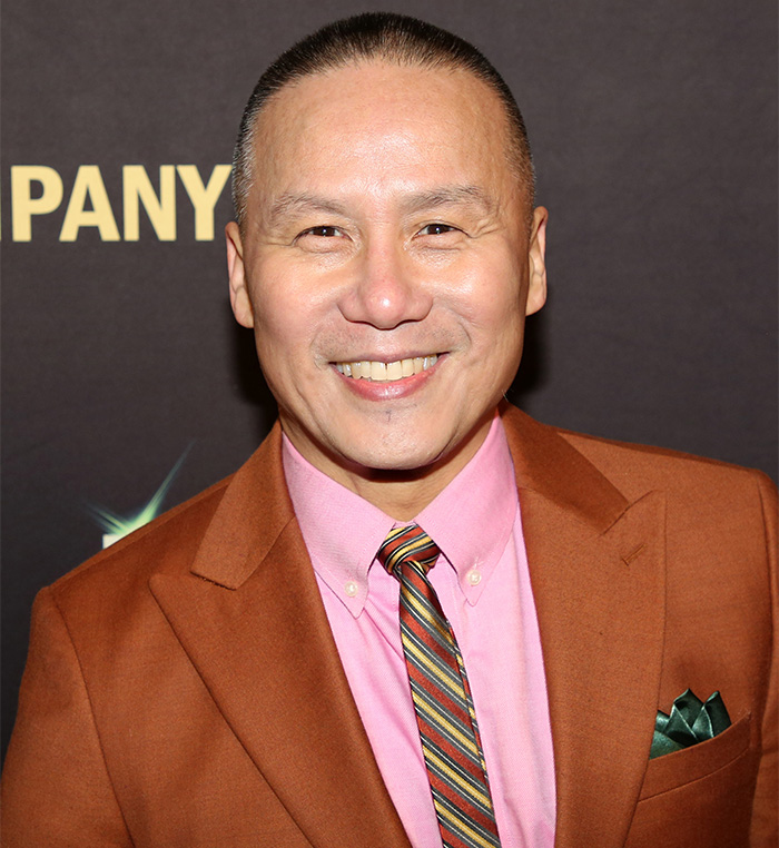 BD Wong, Jurassic World star, smiling in a brown suit and striped tie at a public event against a dark backdrop. BD Wong, Jurassic World star, smiling in a brown suit and striped tie at a public event against a dark backdrop.