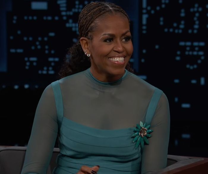 Michelle Obama smiling with bold makeup and braided hair during a TV interview praising makeup artist. Michelle Obama smiling with bold makeup and braided hair during a TV interview praising makeup artist.