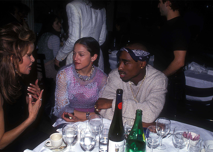 Rarely-seen pop culture shot of three people having a conversation around a dinner table with drinks and glasses.