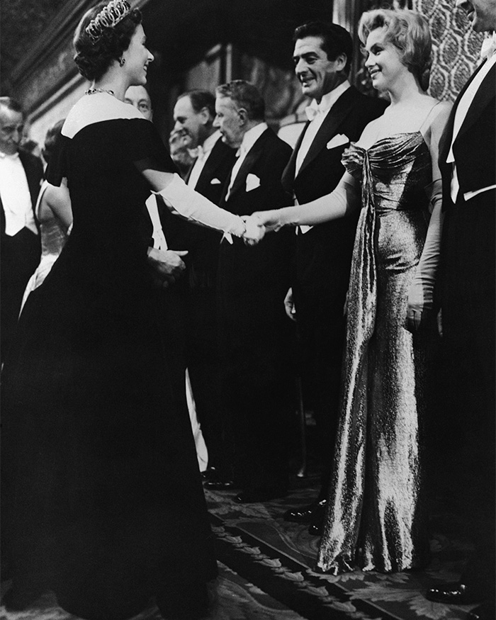 Rarely-seen pop culture shot of Marilyn Monroe shaking hands with Queen Elizabeth II at a formal event in black and white.