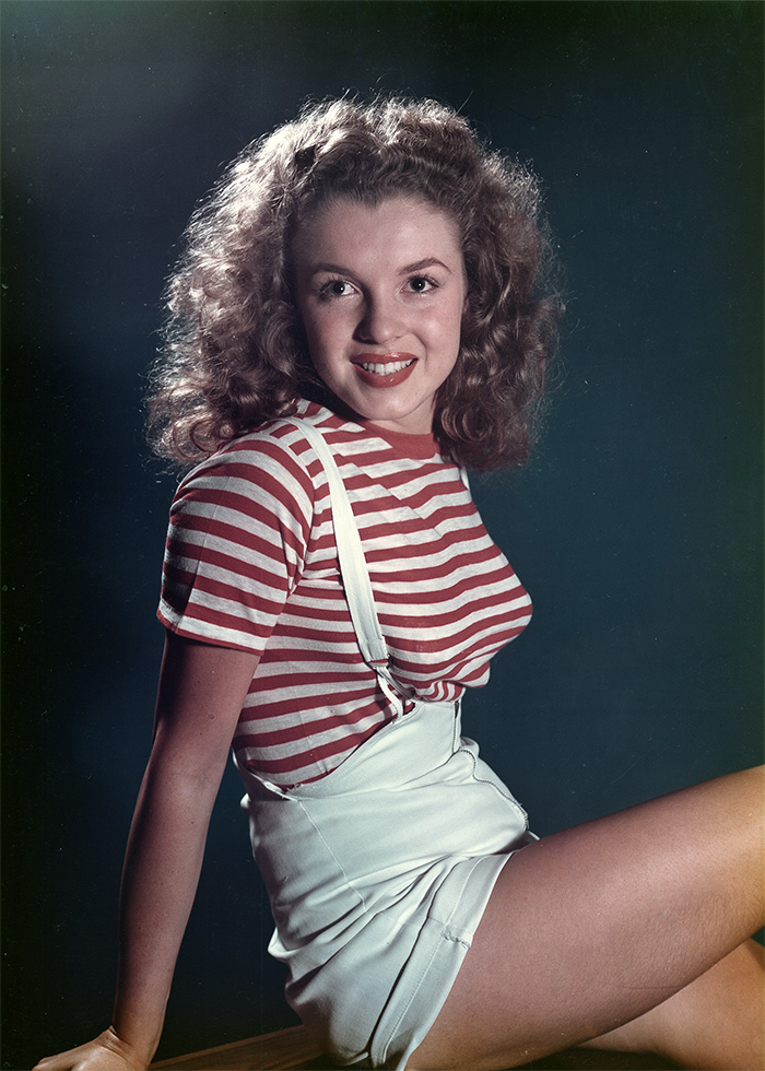 Young woman with curly hair in vintage striped shirt and white overalls, a rare pop culture shot from mid-20th century.