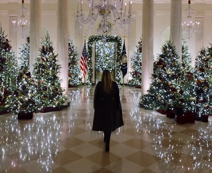 Melania Trump walking through a hall decorated with Christmas trees and sparkling lights for holiday season. Melania Trump walking through a hall decorated with Christmas trees and sparkling lights for holiday season.