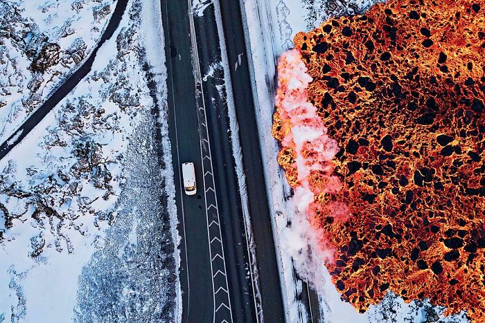 Aerial view of a vehicle on a snowy road near vivid molten lava flow in stunning nature wildlife photo.