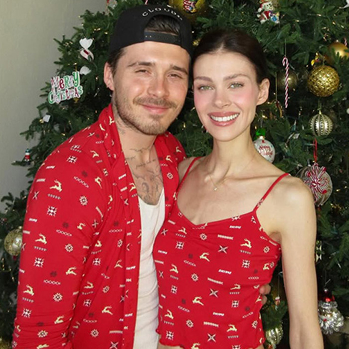 Brooklyn and Nicola Peltz posing in matching red Christmas outfits by a decorated holiday tree.
