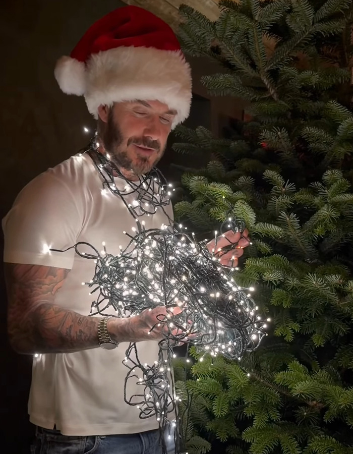 Man wearing Santa hat holding tangled Christmas lights near a tree, related to Brooklyn&rsquo;s wife Nicola Peltz and Victoria posts.