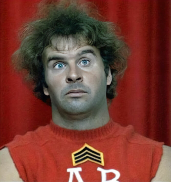 Man with messy hair and intense blue eyes wearing a red sleeveless shirt representing once famous regular job.