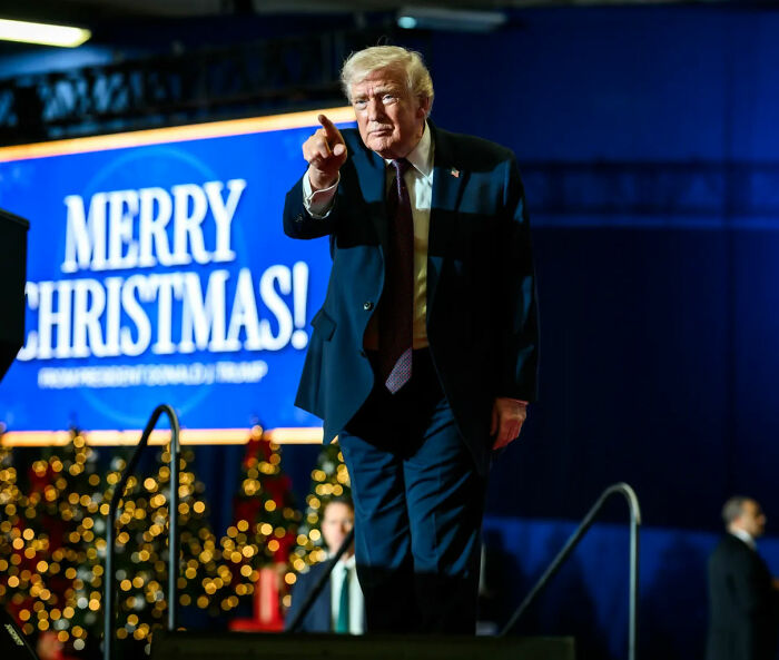 Donald Trump pointing during a Christmas event with a Merry Christmas sign, related to bad Santa comments controversy.