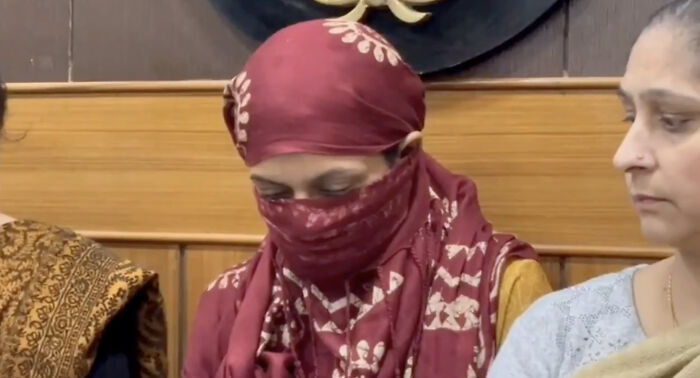 Woman wearing maroon headscarf and face covering sitting beside another woman in emotional setting revealing wedding tragedy pattern. Woman wearing maroon headscarf and face covering sitting beside another woman in emotional setting revealing wedding tragedy pattern.