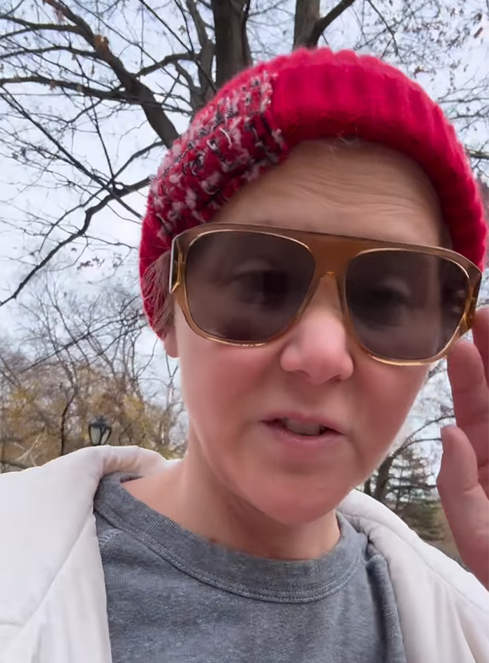 Woman wearing oversized sunglasses and a red knit hat, outdoors in winter, discussing plastic surgeon's perspective on wrinkle-free photos. Woman wearing oversized sunglasses and a red knit hat, outdoors in winter, discussing plastic surgeon's perspective on wrinkle-free photos.