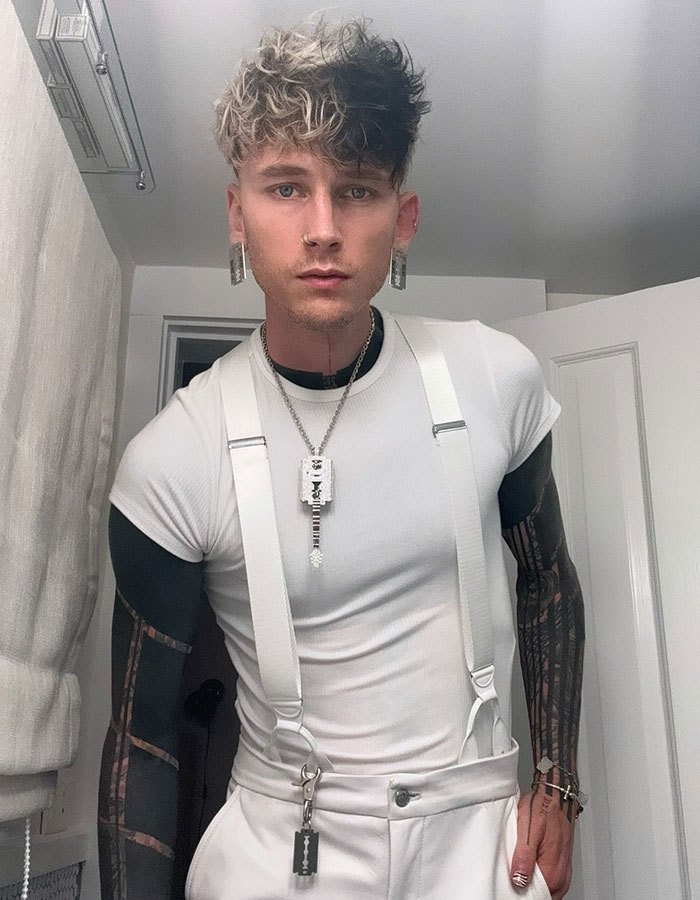 Machine Gun Kelly posing indoors wearing white suspenders and jewelry, related to boy band dancing viral reaction.