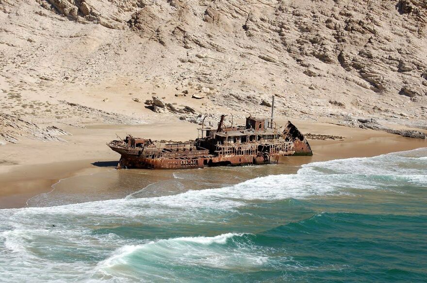 Rusty abandoned shipwreck on a remote beach with steep rocky cliffs, illustrating dangerous places in the world to visit.
