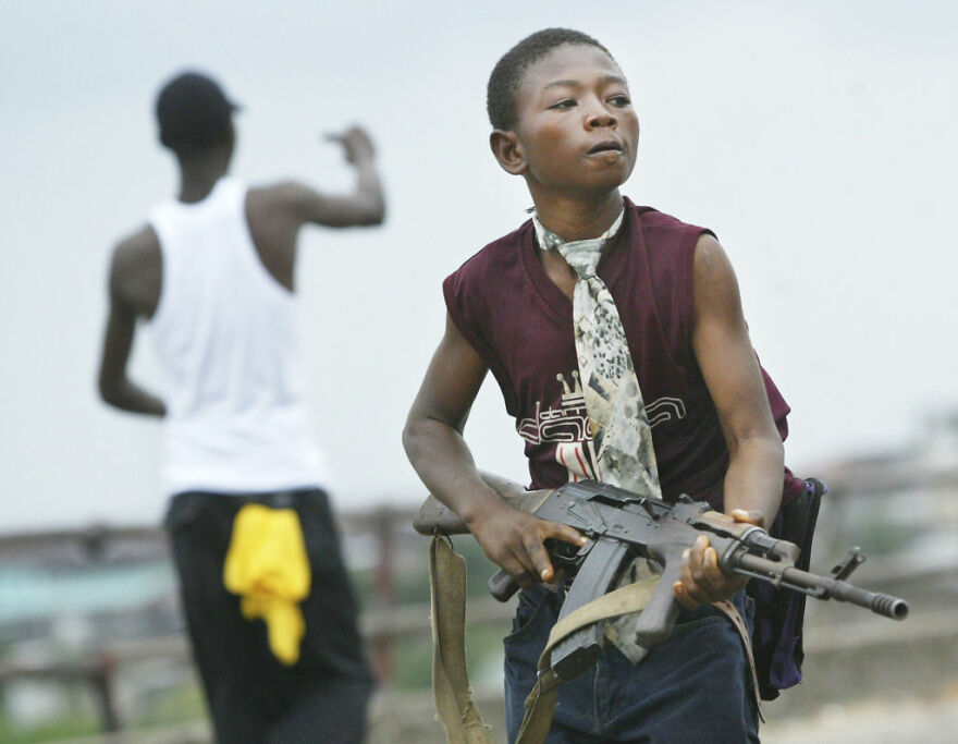 Young boy holding a rifle in a tense setting, illustrating dangers in some of the most dangerous places to visit.