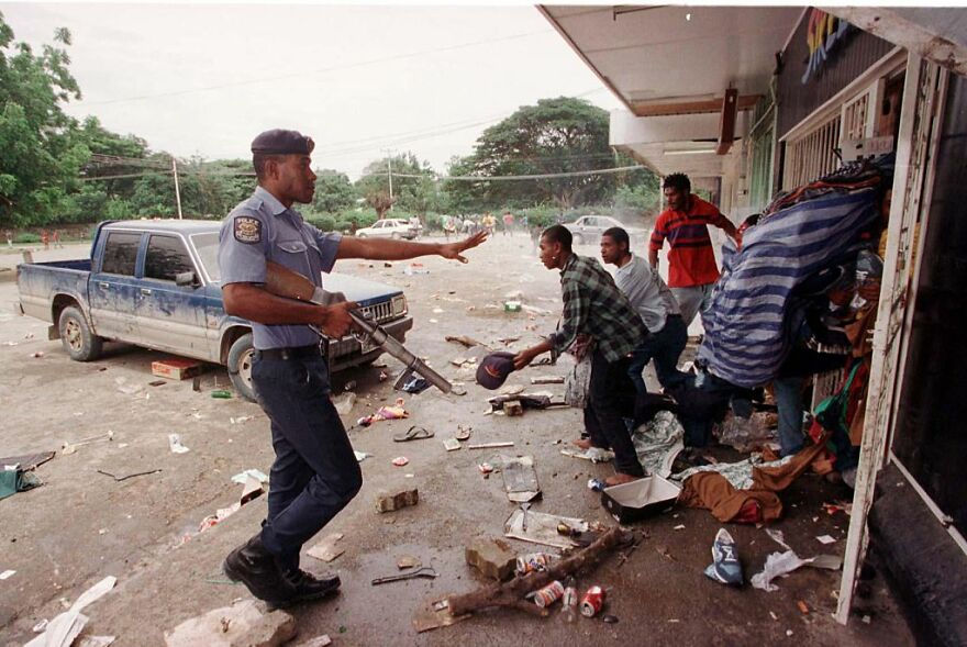 Police officer with a gun confronting civilians amid debris in one of the most dangerous places in the world to visit now