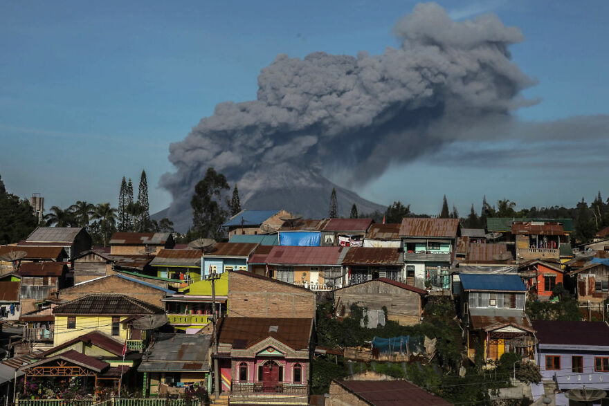Volcanic eruption near village with houses, illustrating one of the most dangerous places in the world to visit.