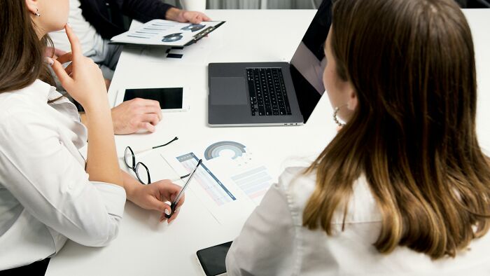 Two women in a meeting reviewing charts and data on paper and laptop, deciding how to stay calm in scenarios.