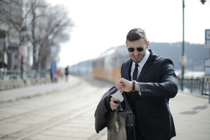 Man in a suit looking stressed while checking his watch at an outdoor train station, illustrating staying calm or losing it.