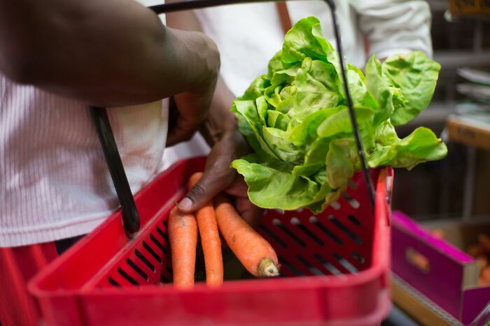 Person placing fresh carrots and lettuce into a red shopping basket while deciding how to stay calm or lose it.