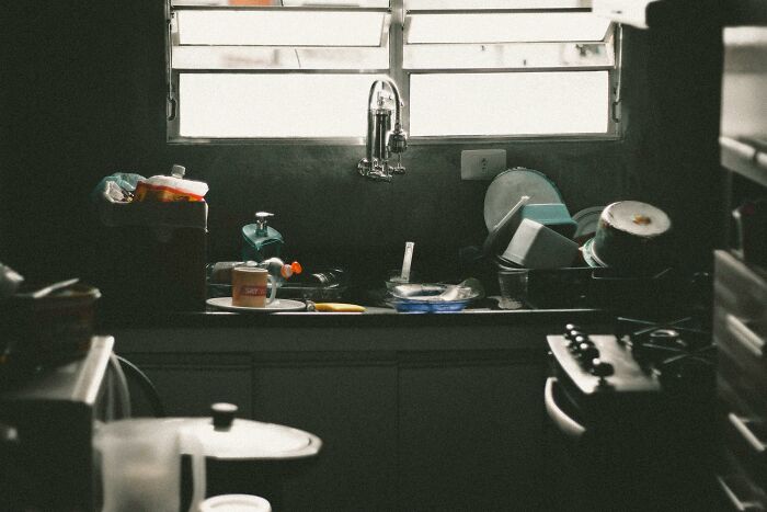 Dimly lit kitchen sink filled with dirty dishes under a window, illustrating scenarios to stay calm or lose it.