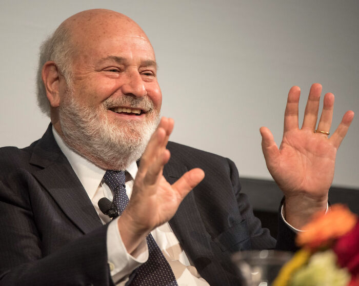 Rob Reiner speaking at an event, smiling and gesturing with hands while wearing a suit and tie. Rob Reiner speaking at an event, smiling and gesturing with hands while wearing a suit and tie.