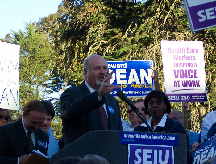 Man speaking at a political rally with SEIU signs, highlighting MAGA hypocrisy and comparisons between Rob Reiner and Charlie Kirk. Man speaking at a political rally with SEIU signs, highlighting MAGA hypocrisy and comparisons between Rob Reiner and Charlie Kirk.