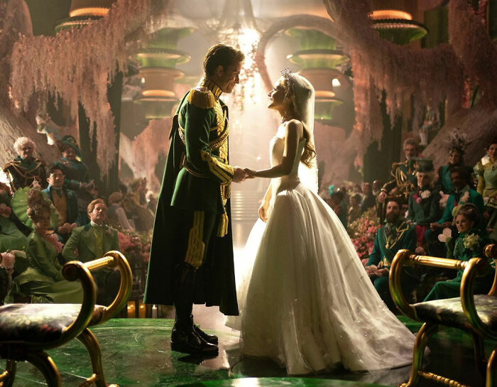 David Corenswet in a period costume holding hands with a bride in a white gown during an elaborate ceremony scene.