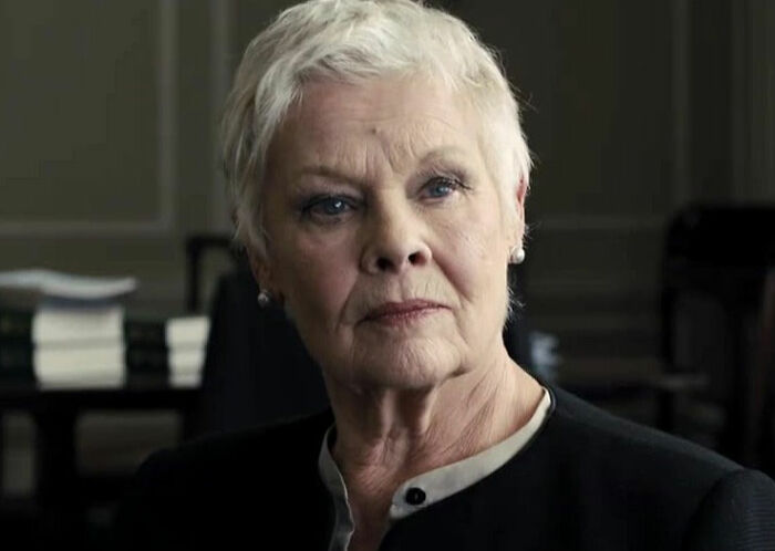 Dame Judi Dench with short white hair and dark clothing, in a serious expression during an indoor interview. Dame Judi Dench with short white hair and dark clothing, in a serious expression during an indoor interview.