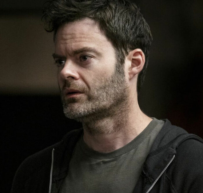 Bill Hader looking serious with scruffy beard and dark hoodie, captured during a tense moment at a social event.