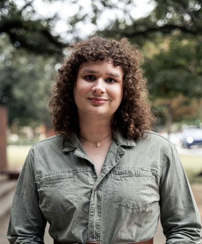 Young student outdoors with curly hair and green shirt, symbolizing essay that got trans instructor removed from university. Young student outdoors with curly hair and green shirt, symbolizing essay that got trans instructor removed from university.