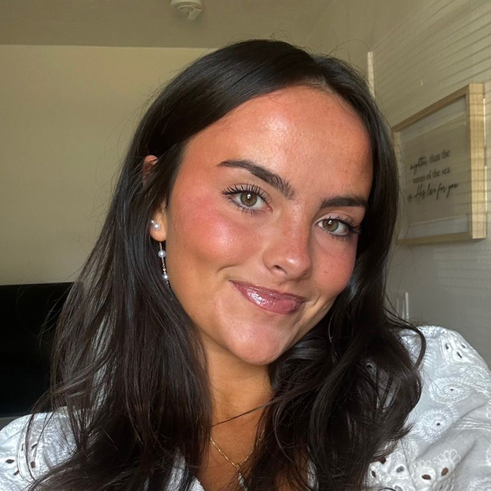 Young woman smiling indoors, representing student anonymously exposing essay details about trans instructor removal. Young woman smiling indoors, representing student anonymously exposing essay details about trans instructor removal.