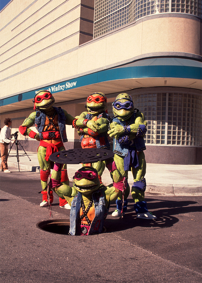 Rarely-seen pop culture shot of Teenage Mutant Ninja Turtles posing on city street near manhole cover.