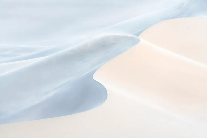 Smooth sand dunes and soft shadows create an abstract, minimal scene showcasing the best nature photography of 2025.