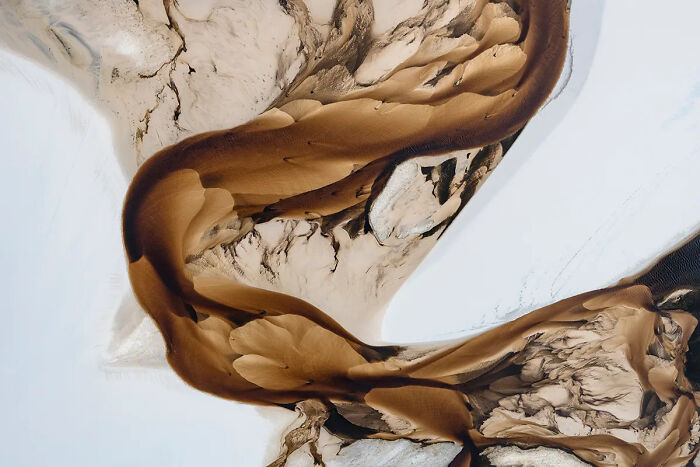 Aerial view of desert dunes flowing into a frozen landscape, showcasing best nature photography of 2025.