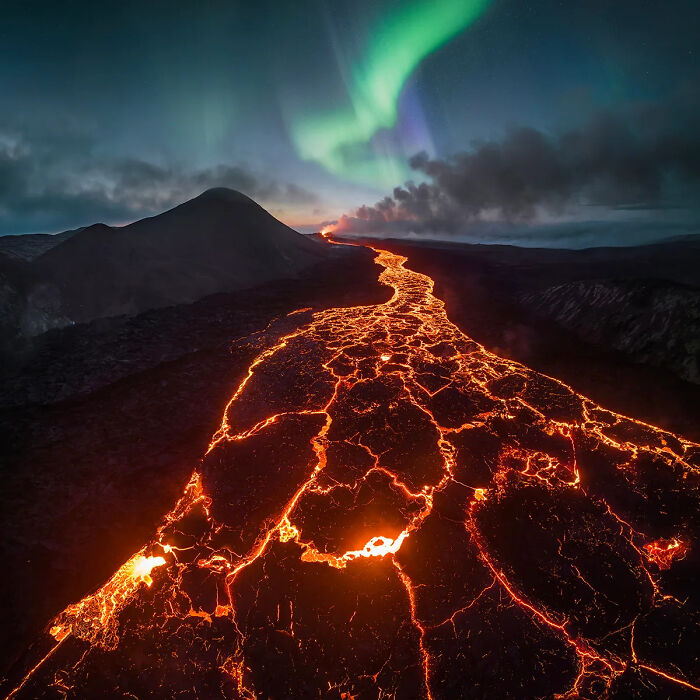 Glowing lava flow under northern lights with a mountain backdrop captured in best nature photography 2025.