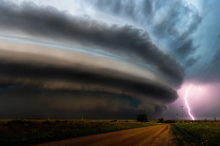 Massive storm cloud formation with lightning strike over rural road captured in best nature photography scene.