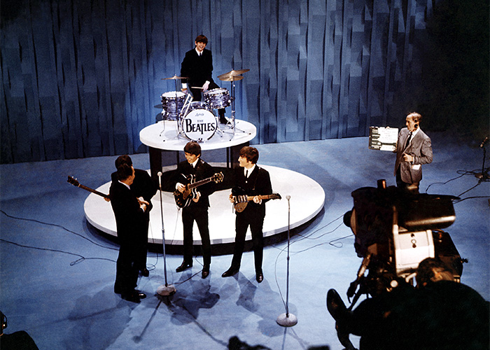 Rare pop culture shot of the Beatles performing on a vintage TV show stage with classic instruments and cameras filming.