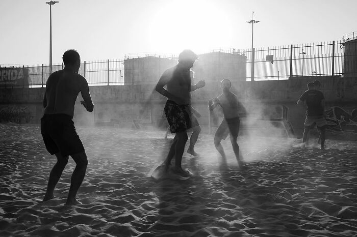 Silhouettes of people playing and moving on sandy ground creating magical street moments in daily life at sunset.